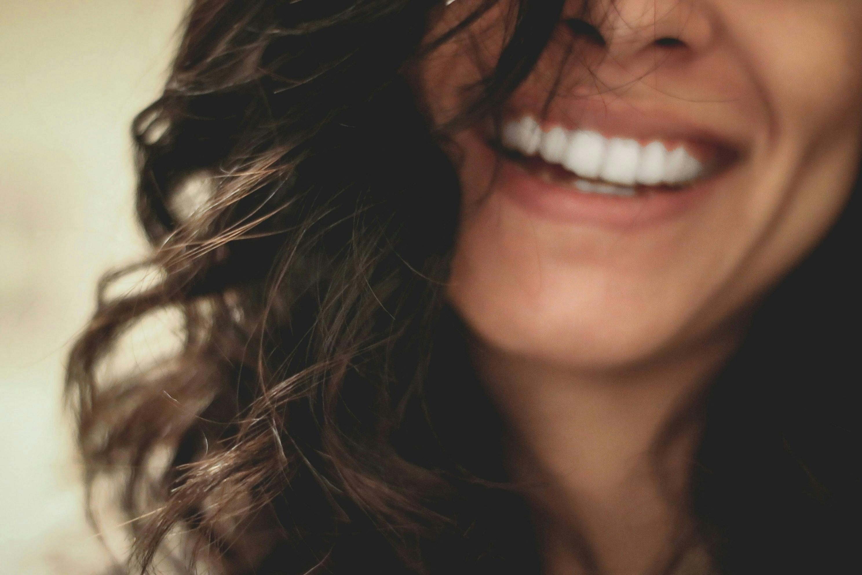 A woman with curly hair smiling broadly, showcasing her perfect white teeth after dental treatment